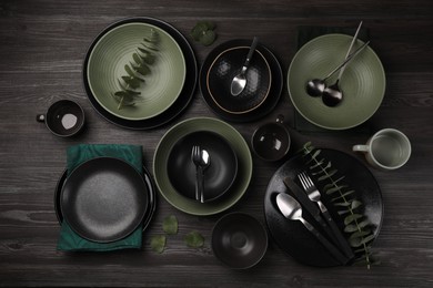 Stylish table setting with cutlery and eucalyptus branches on dark wooden background, flat lay