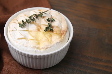 Tasty baked camembert and thyme in bowl on wooden table, closeup. Space for text