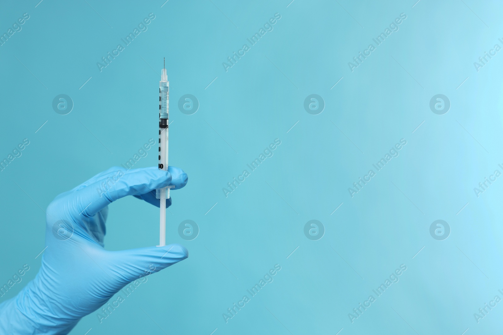 Photo of Doctor holding syringe on light blue background, closeup. Space for text