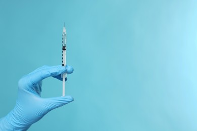 Doctor holding syringe on light blue background, closeup. Space for text