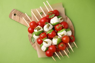 Photo of Caprese skewers with tomatoes, mozzarella balls, basil and pesto sauce on green background, top view