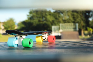 Modern black skateboard with colorful wheels on top of ramp outdoors, space for text