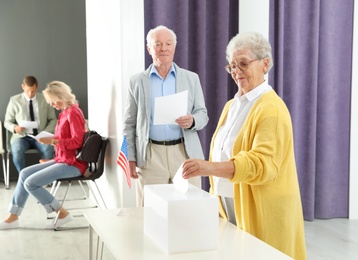 Elderly woman putting ballot paper into box at polling station