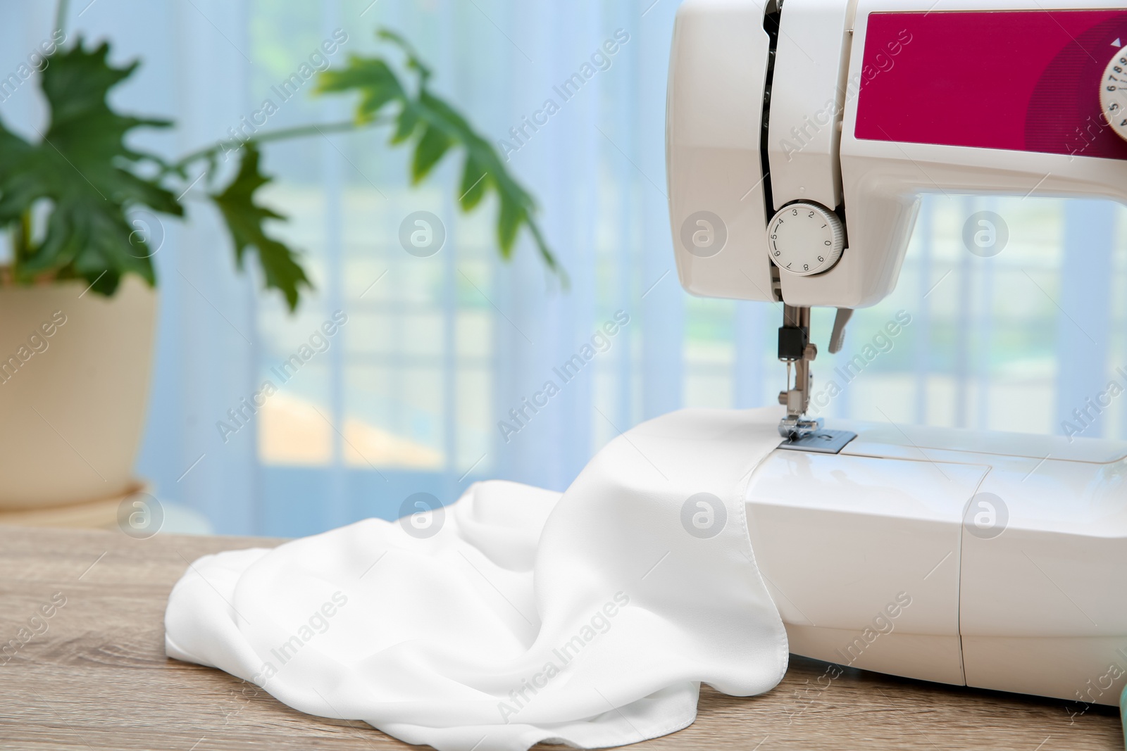 Photo of Sewing machine with textile on table near window