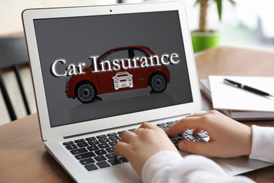 Woman using laptop for car insurance at table indoors, closeup