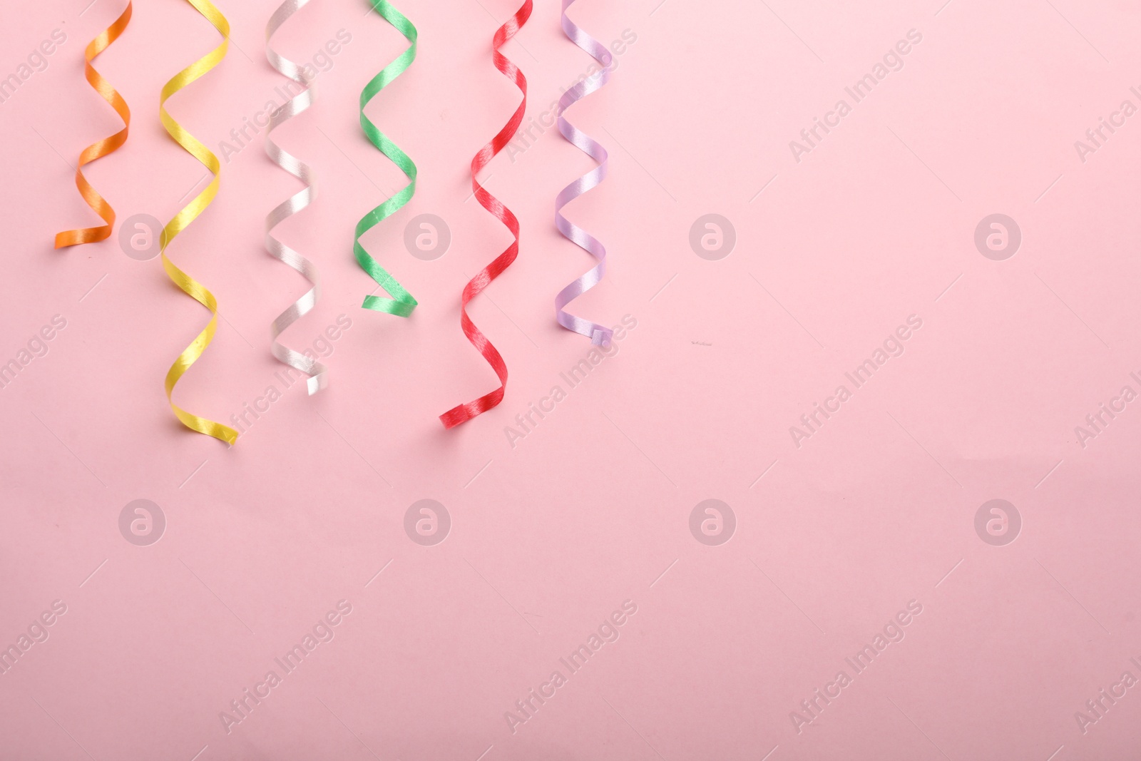 Photo of Colorful serpentine streamers on pink background, flat lay. Space for text