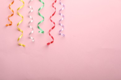 Colorful serpentine streamers on pink background, flat lay. Space for text