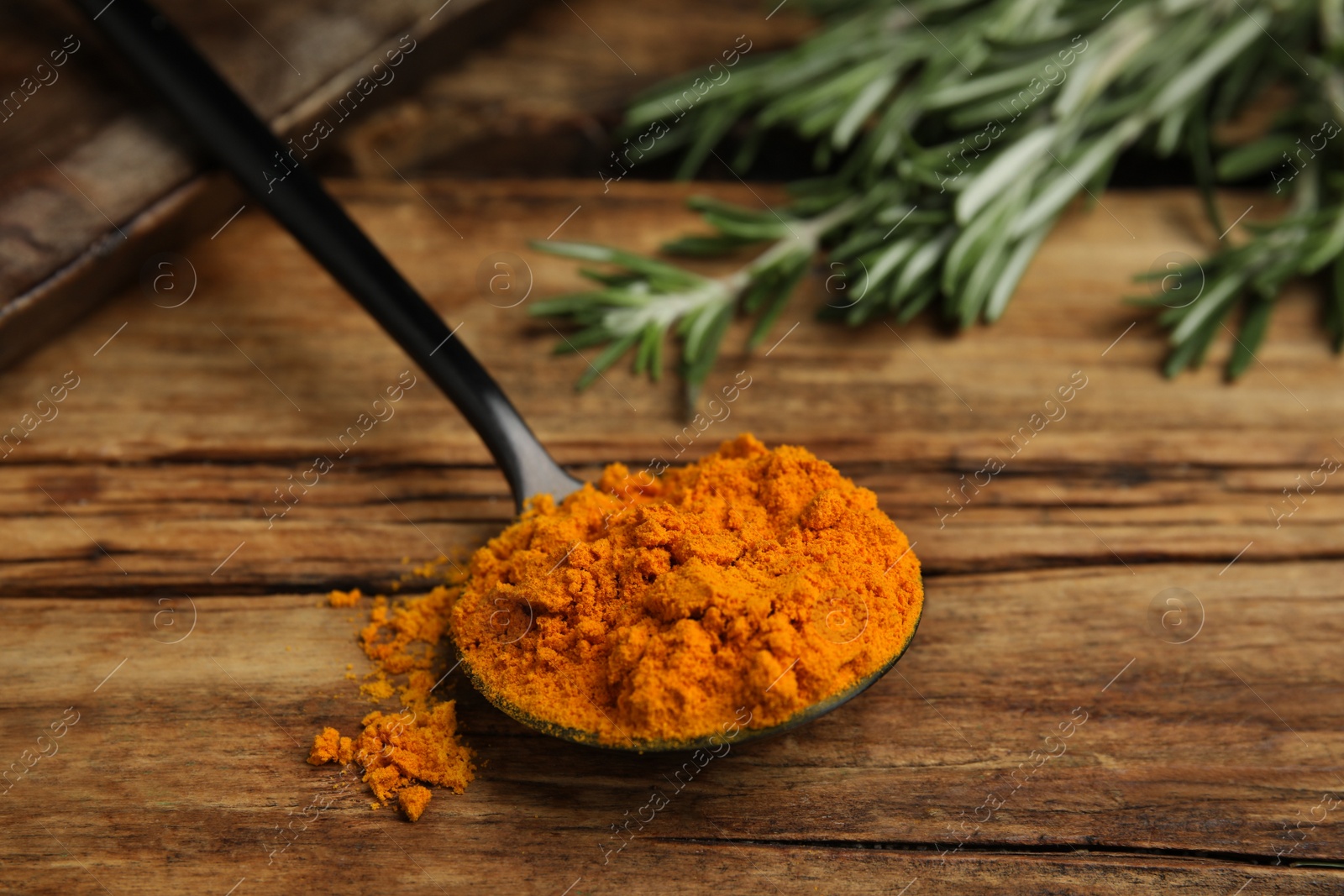 Photo of Spoon with saffron powder and rosemary on wooden table, closeup