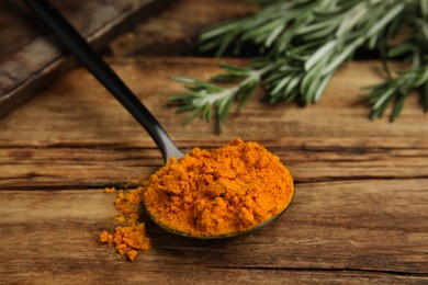 Photo of Spoon with saffron powder and rosemary on wooden table, closeup