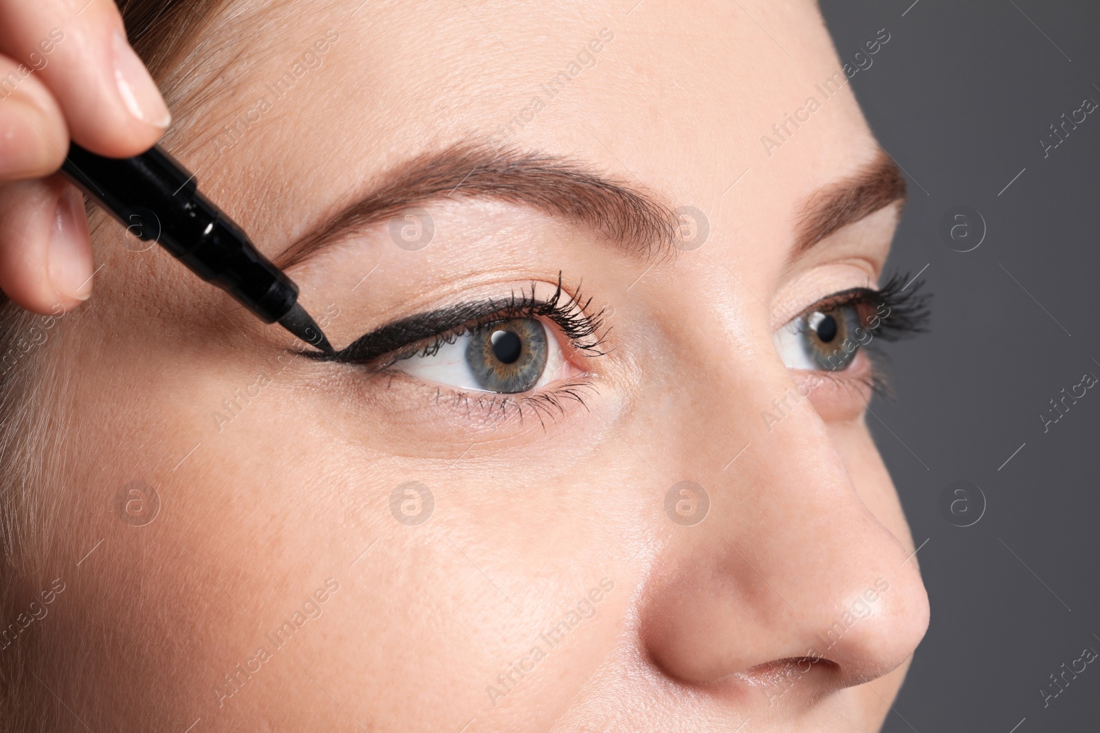 Photo of Artist applying black eyeliner onto woman's face on grey background, closeup