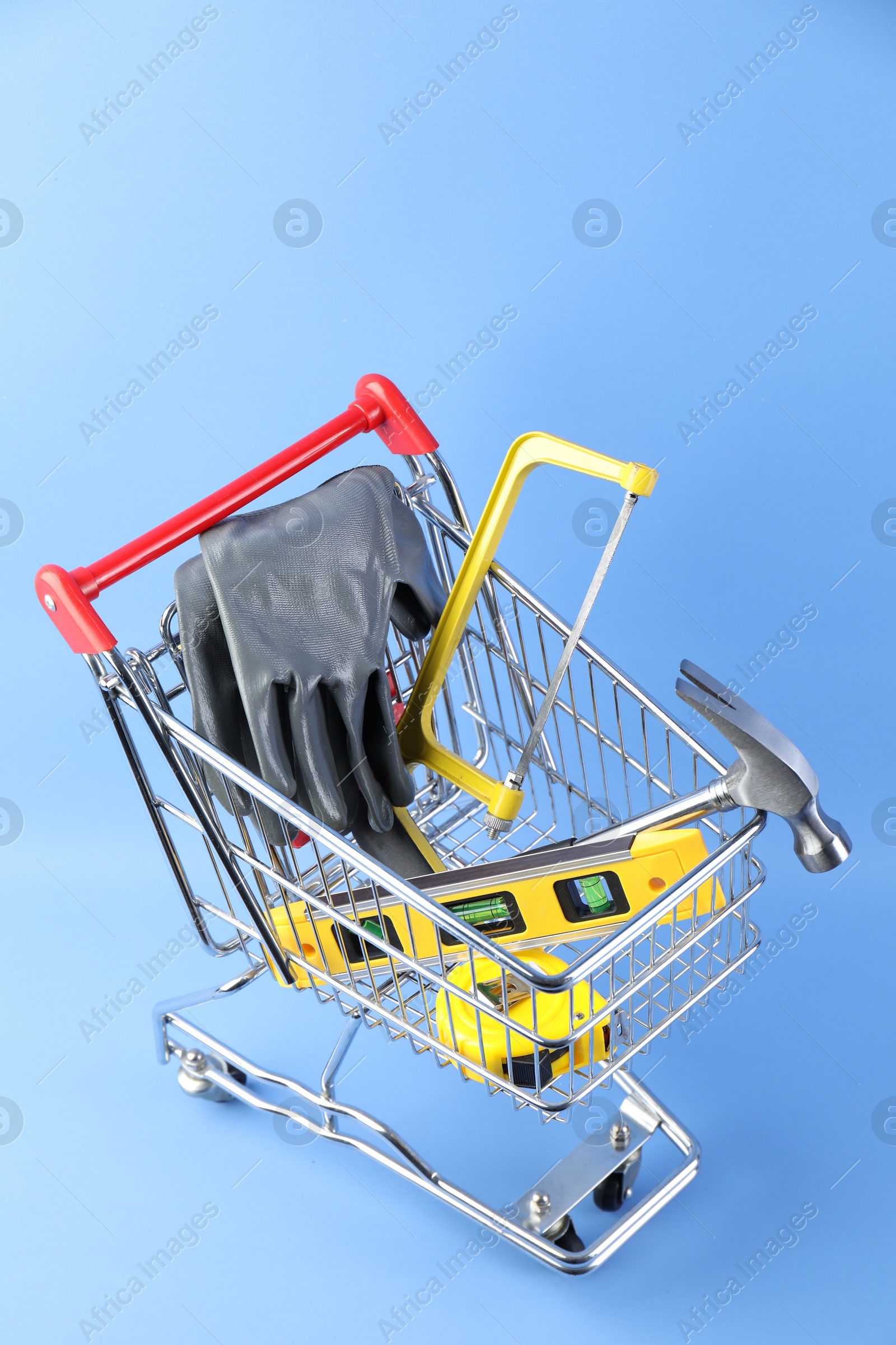 Photo of Small shopping cart with set of construction tools and gloves on light blue background