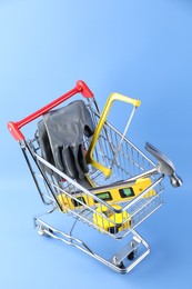 Small shopping cart with set of construction tools and gloves on light blue background