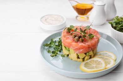 Tasty salmon tartare with avocado, lemon, capers and microgreens on white wooden table. Space for text