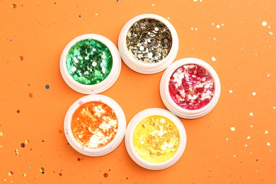 Photo of Colorful shiny glitter in jars on orange background, flat lay