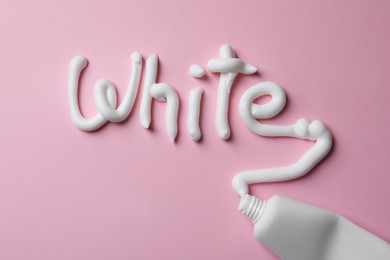 Photo of Word White written with toothpaste and tube on pink background, top view