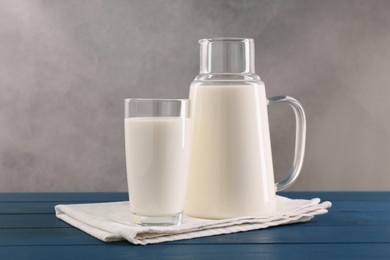 Photo of Carafe and glass of fresh milk on blue wooden table