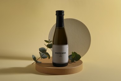 Photo of Bottle of delicious white wine and eucalyptus branches on beige background
