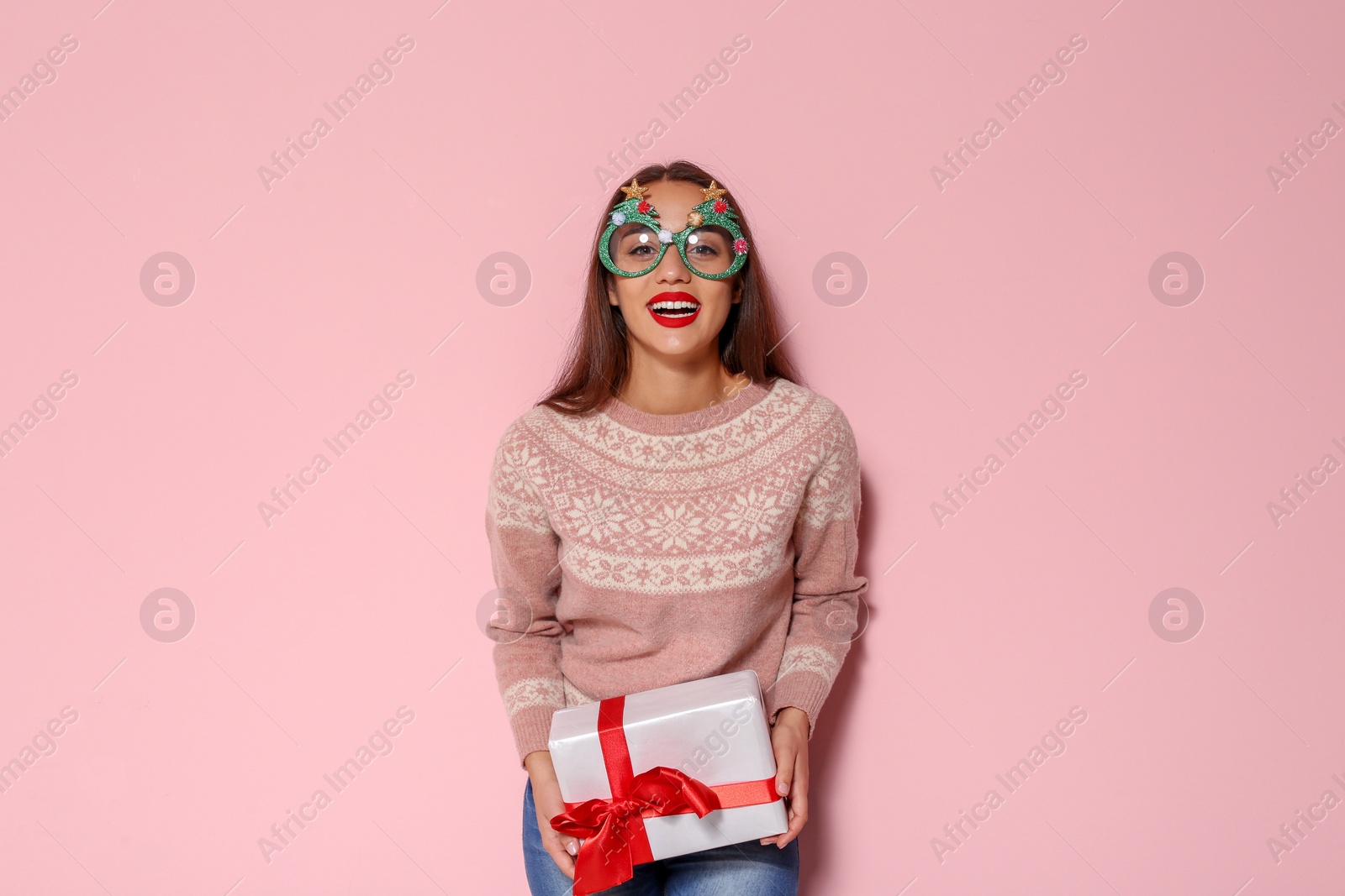 Photo of Young woman in warm sweater with Christmas gift and party glasses on color background