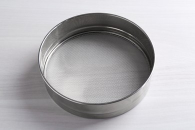 Photo of One metal sieve on white wooden table. Cooking utensil