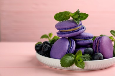 Photo of Delicious macarons, mint and blueberries on pink wooden table, closeup