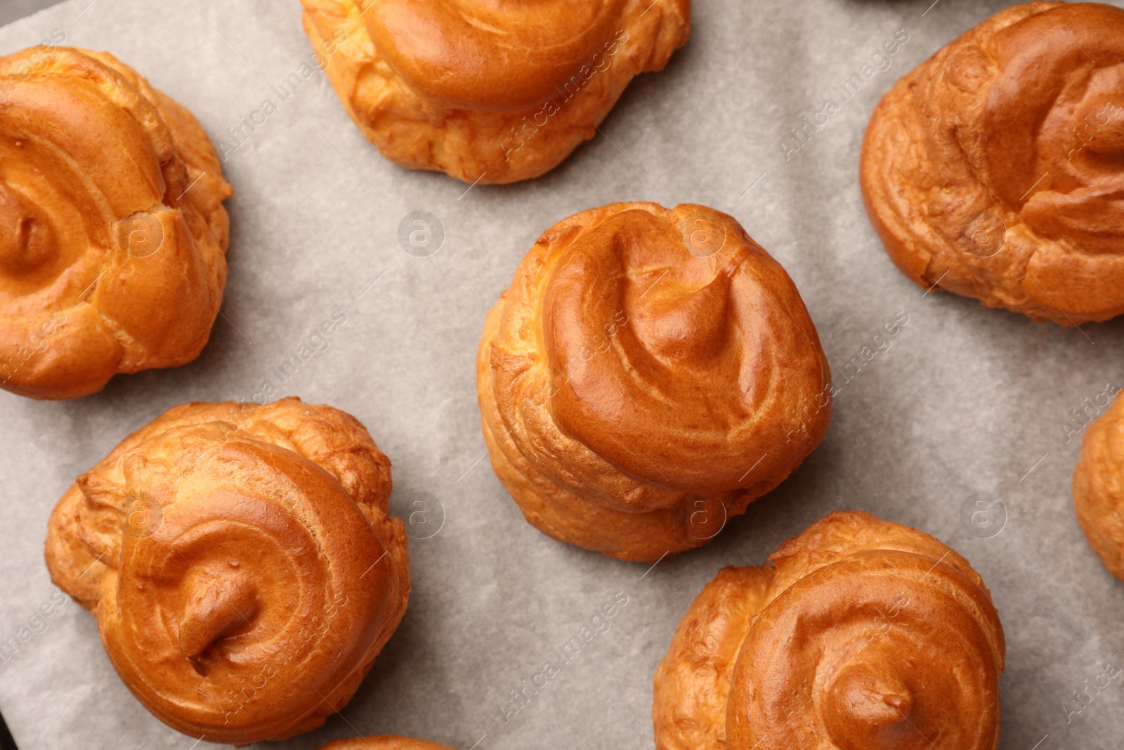 Photo of Delicious profiteroles on parchment paper, flat lay