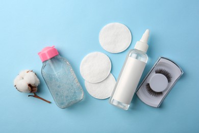 Photo of Bottles of makeup removers, cotton flower, pads and false eyelashes on light blue background, flat lay