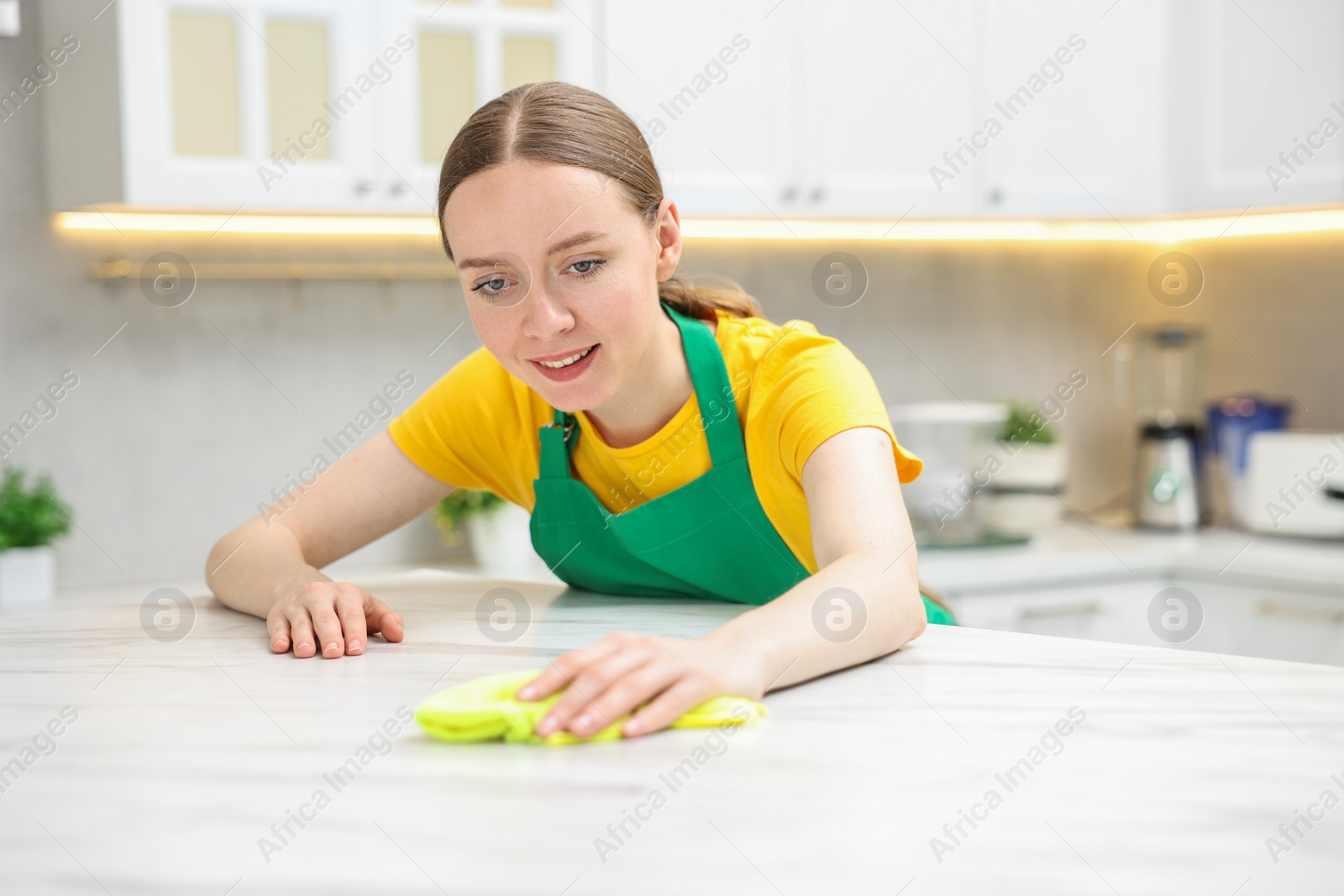 Photo of Woman cleaning white marble table with rag in kitchen