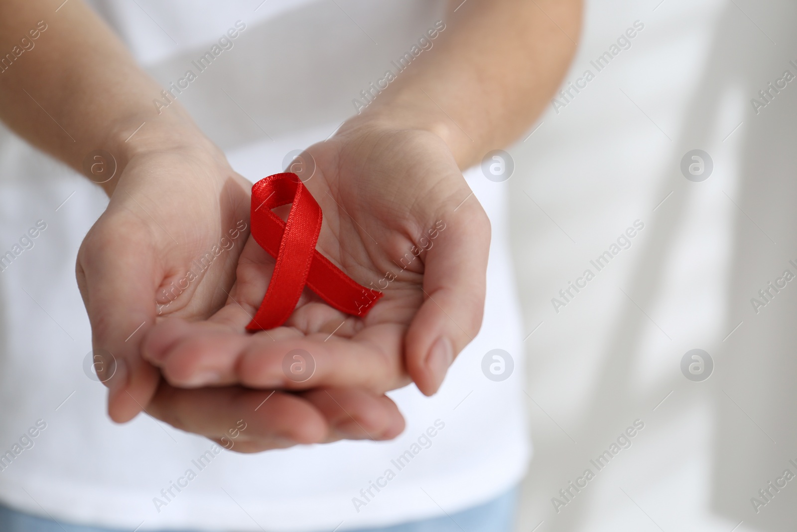 Photo of Woman holding red awareness ribbon on light background, closeup with space for text. World AIDS disease day