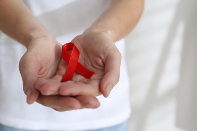 Photo of Woman holding red awareness ribbon on light background, closeup with space for text. World AIDS disease day