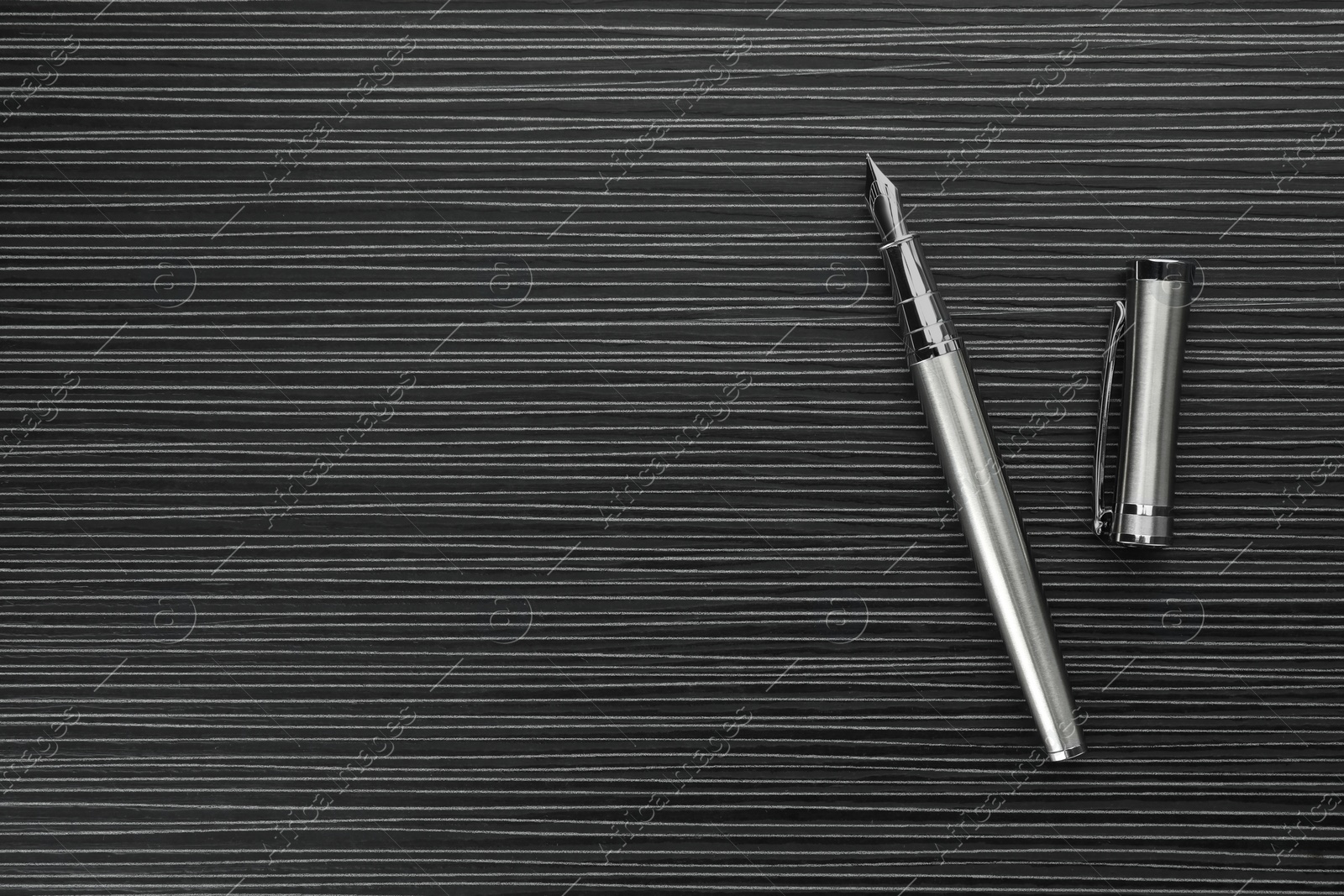 Photo of Stylish silver fountain pen on black wooden table, top view. Space for text