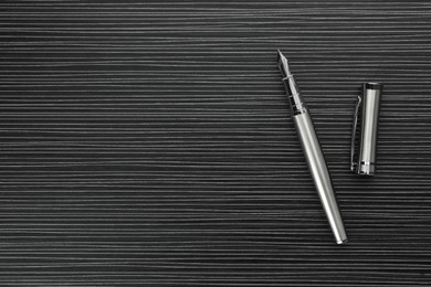 Stylish silver fountain pen on black wooden table, top view. Space for text