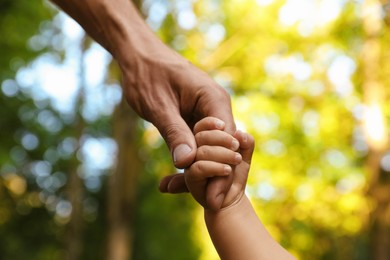Photo of Daughter holding father's hand outdoors, closeup. Happy family