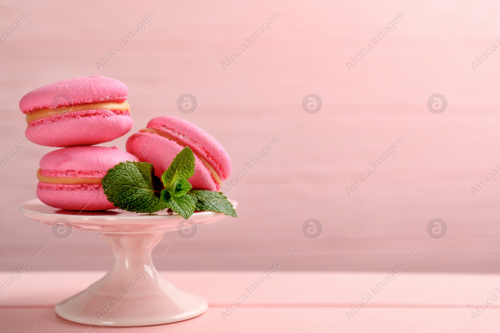 Photo of Delicious macarons and mint on pink wooden table. Space for text