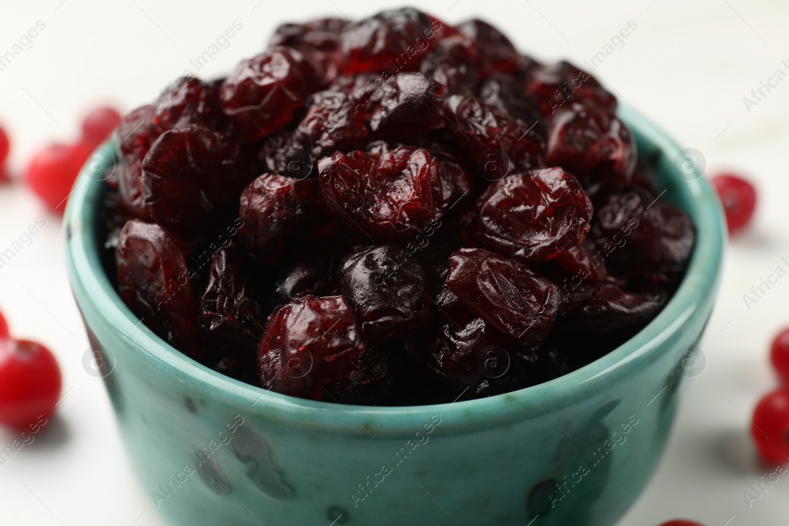 Photo of Tasty dried cranberries in bowl on white table, closeup