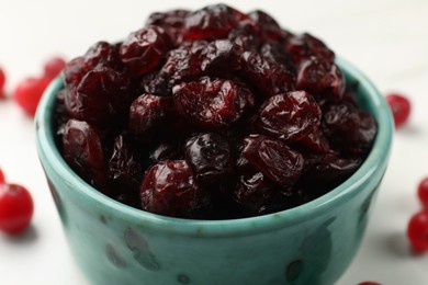 Tasty dried cranberries in bowl on white table, closeup