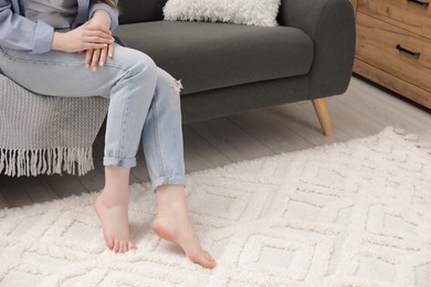 Photo of Woman sitting on sofa near beige carpet indoors, closeup. Space for text