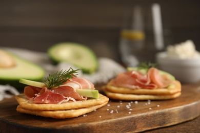 Photo of Delicious crackers with avocado, prosciutto and dill on wooden board, closeup