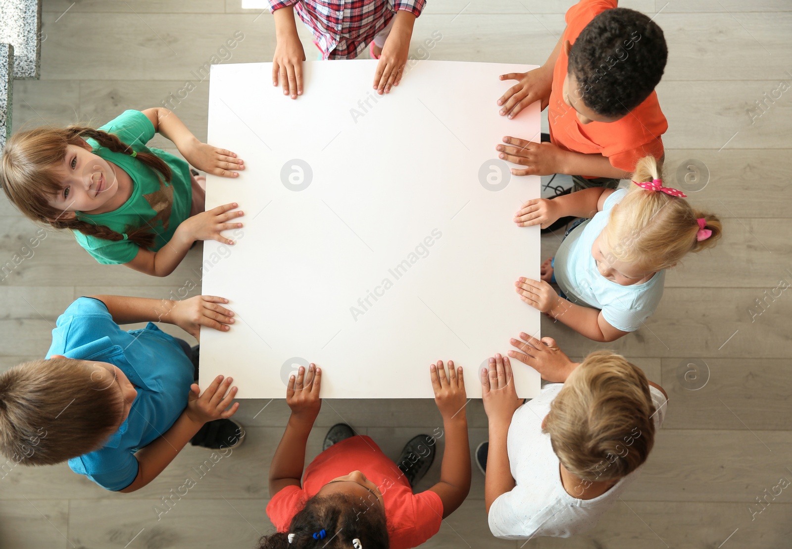 Photo of Little children holding sheet of paper in hands together indoors, top view. Unity concept