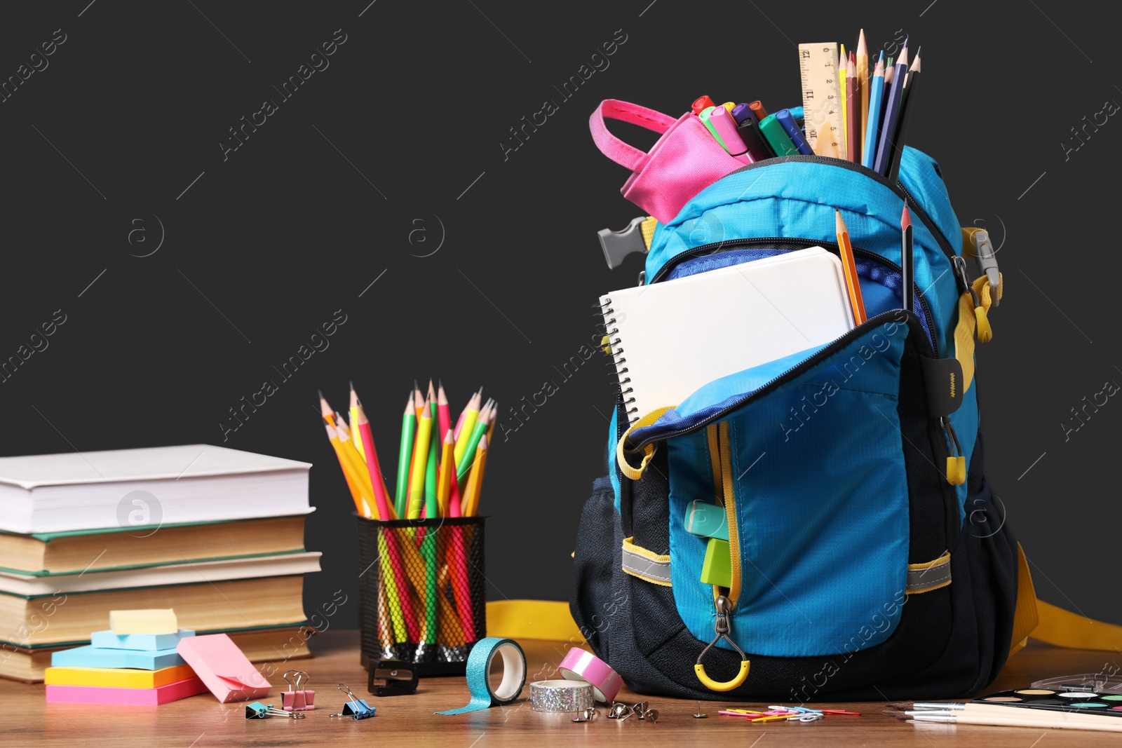 Photo of Backpack with different school stationery on wooden table near blackboard, space for text