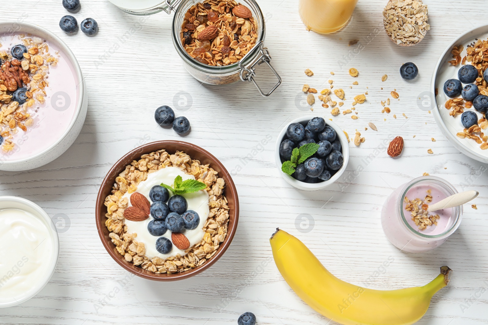 Photo of Different bowls of oatmeal with yogurt and blueberries on white wooden table, flat lay