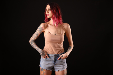 Photo of Beautiful woman with tattoos on body against black background