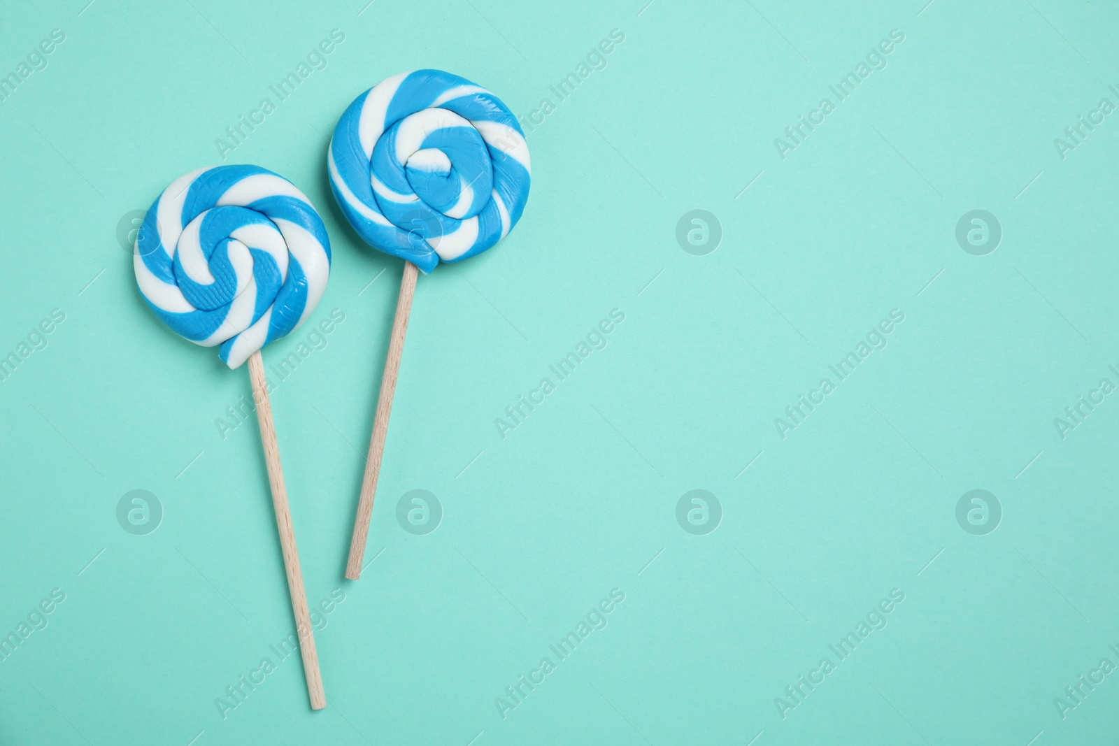 Photo of Sticks with bright lollipops on turquoise background, flat lay. Space for text
