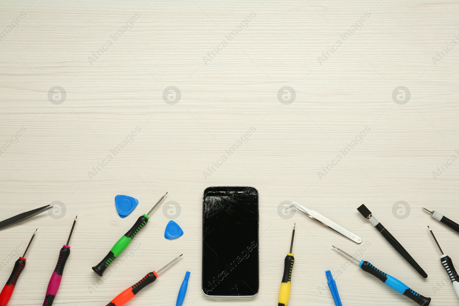 Photo of Damaged smartphone and repair tool set on white wooden background, flat lay. Space for text