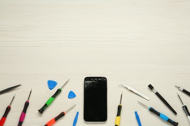 Photo of Damaged smartphone and repair tool set on white wooden background, flat lay. Space for text