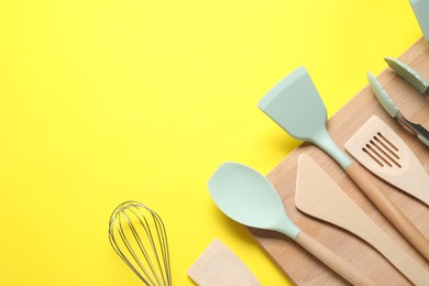 Photo of Different spatulas, whisk and tongs on yellow background, flat lay. Space for text