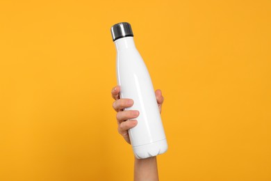 Photo of Woman holding thermo bottle of drink on orange background, closeup