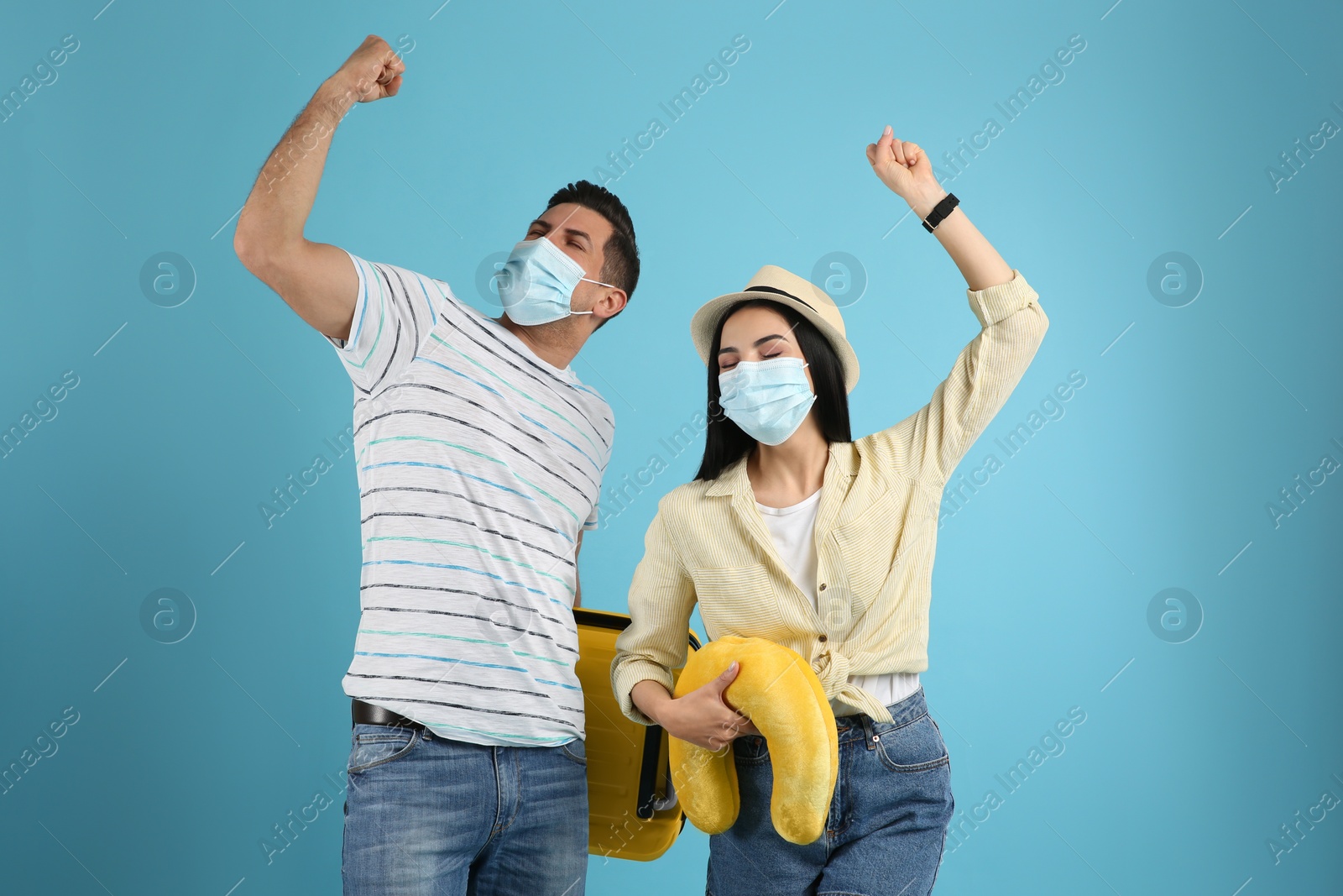 Photo of Couple of tourists in medical masks on light blue background. Travelling during coronavirus pandemic