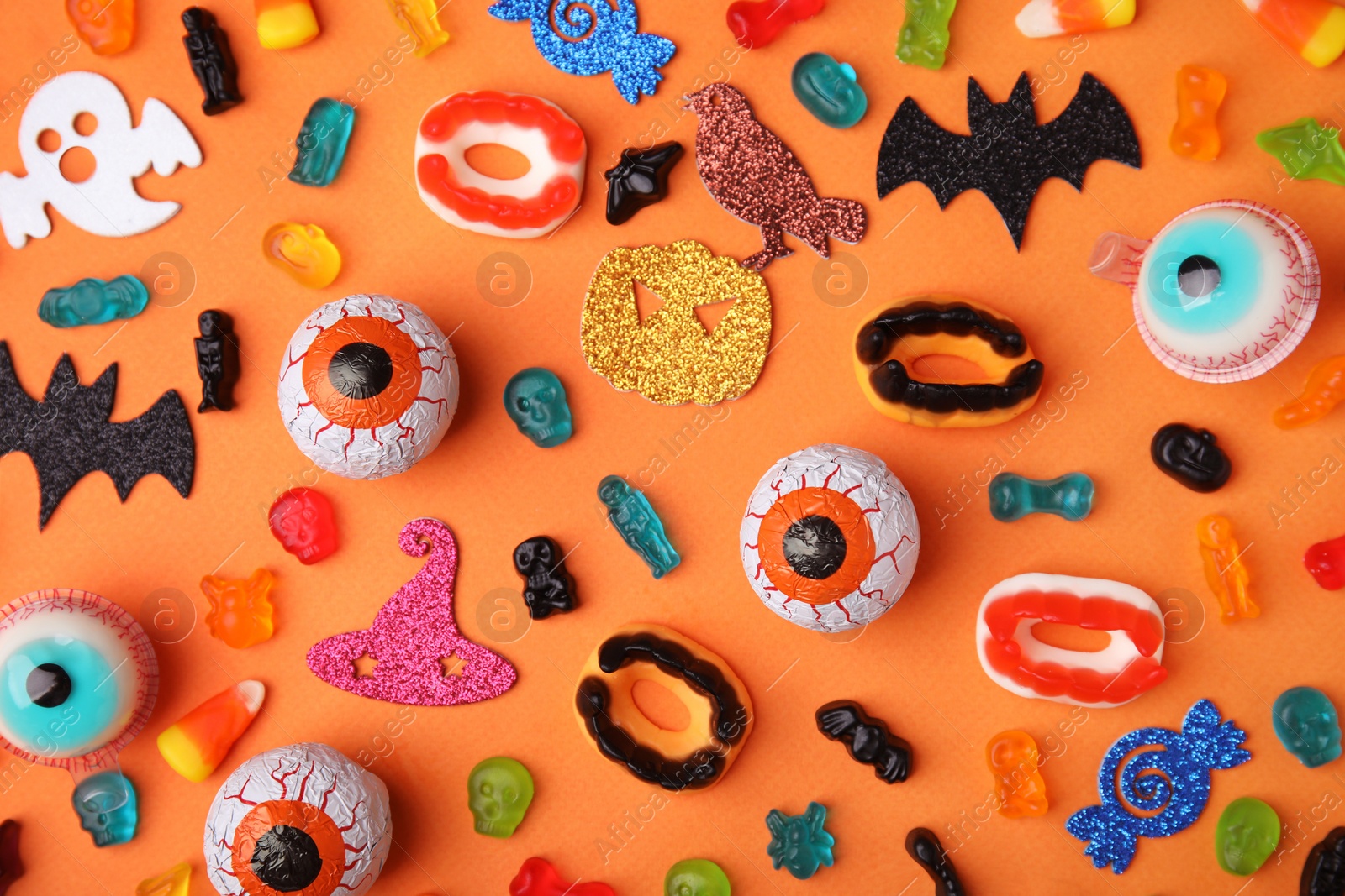 Photo of Tasty candies and Halloween decorations on orange background, flat lay
