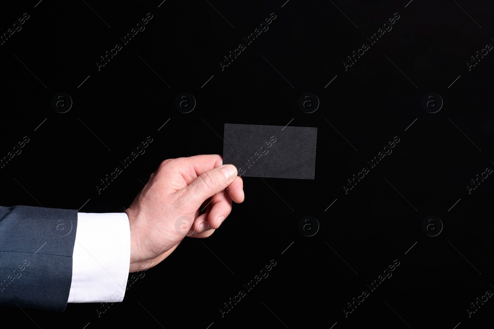 Photo of Businessman holding blank business card on black background, closeup. Space for text