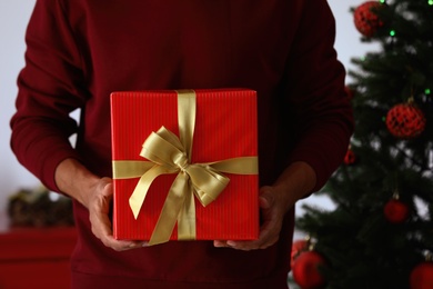 Photo of Man in red sweater holding Christmas gift at home, closeup